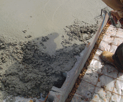 Edge of concrete slab being poured, with anchor bolt and header blocks.
