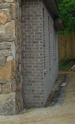 Shingles laid on the ground along the brick wall, to catch water falling from roof.